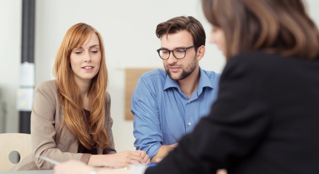 Broker making a presentation to a young couple showing them a document which they are viewing with serious expressions